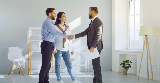 Three people in a modern room, two men and a woman, engaged in a handshake.